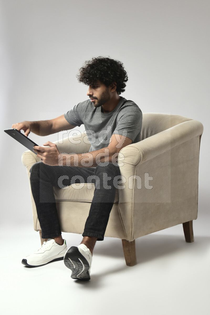 A man wearing casual sitting on a chair browsing on a tablet on white background