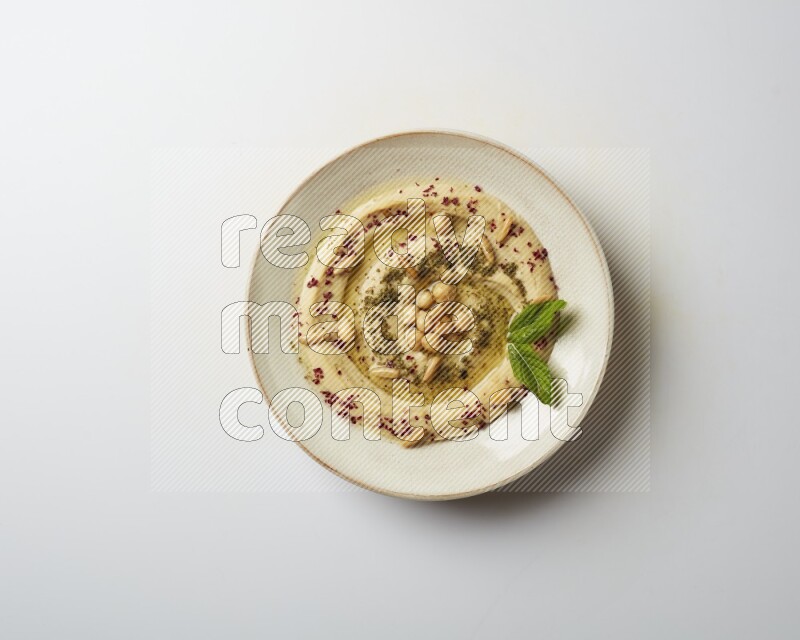 Hummus in a pottry plate garnished with zaatr & sumak on a white background