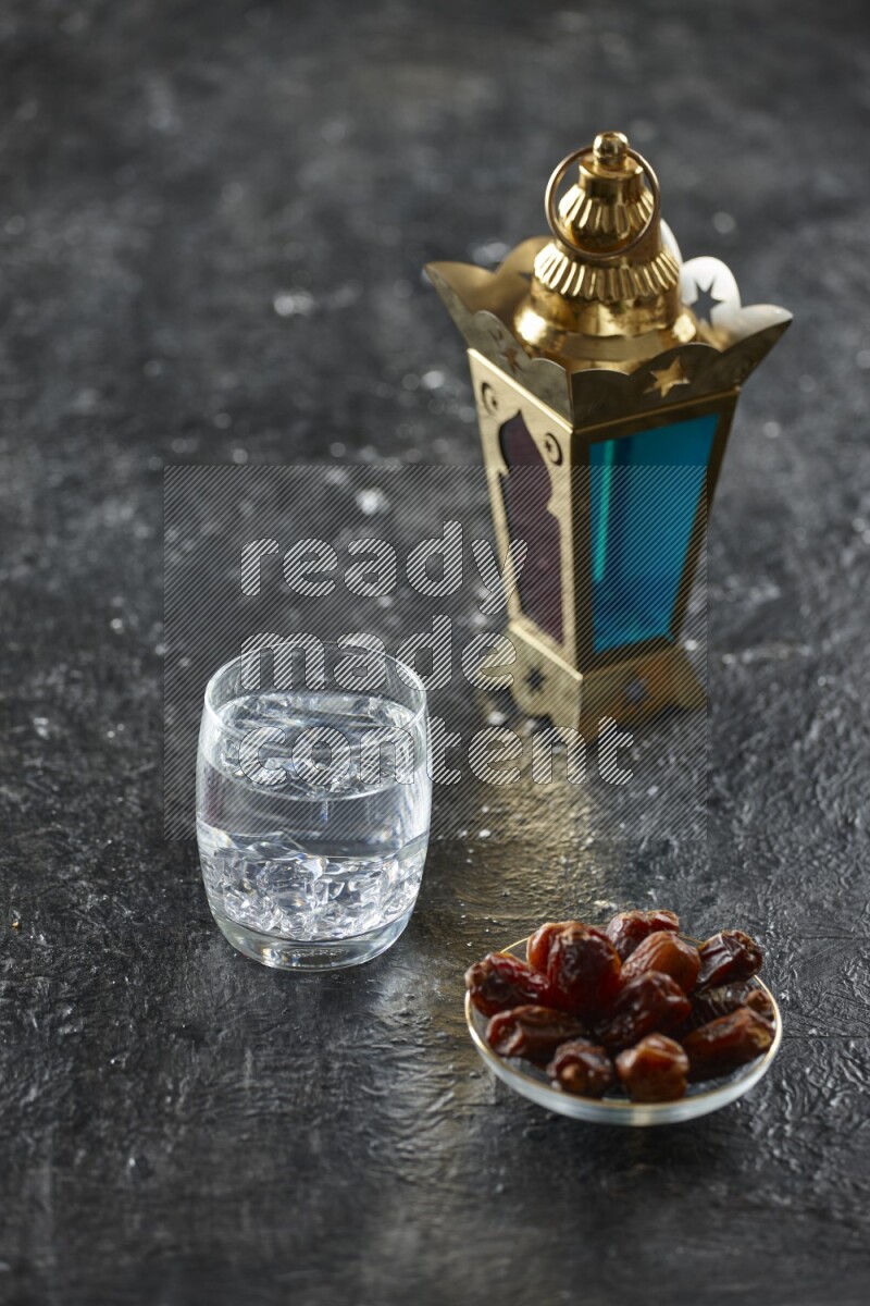 A golden lantern with different drinks, dates, nuts, prayer beads and quran on textured black background