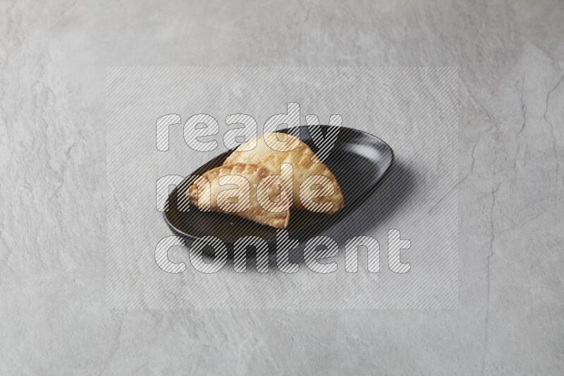 Three fried sambosas in an oval shaped black plate on a gray background