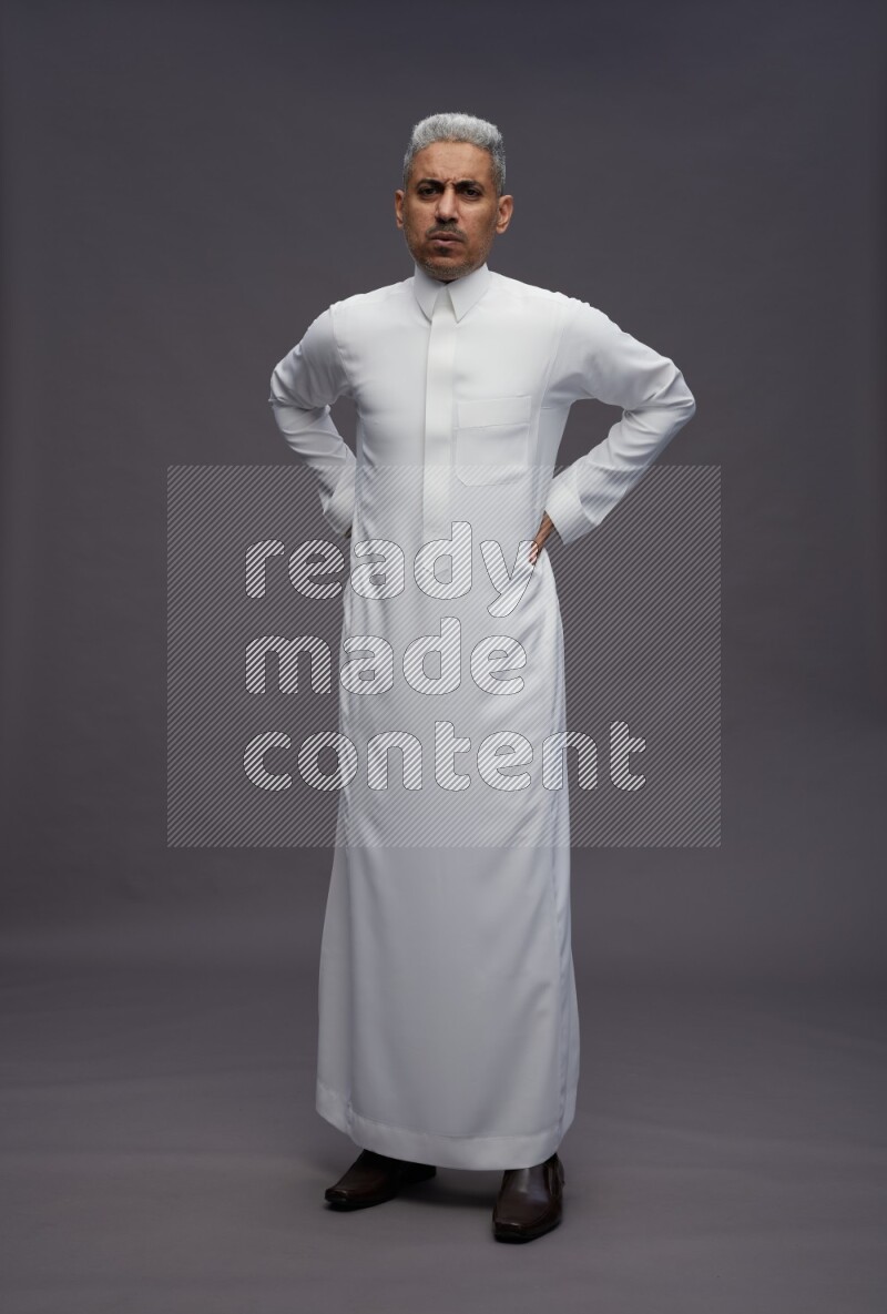 Saudi man wearing thob standing interacting with the camera on gray background