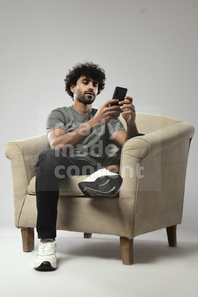 A man wearing casual sitting on a chair browsing on the phone on white background