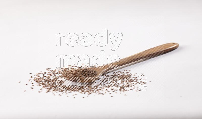 A wooden ladle full of flax seeds on a white flooring