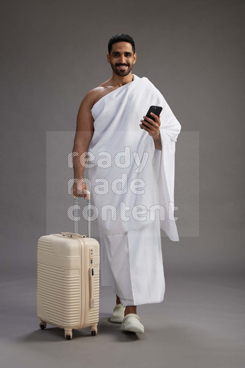 A man wearing Ehram Standing holding traveling bag on gray background