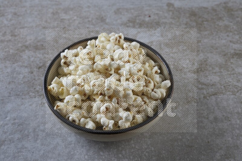 popcorn in a multi-colored pottery bowl on a grey textured countertop