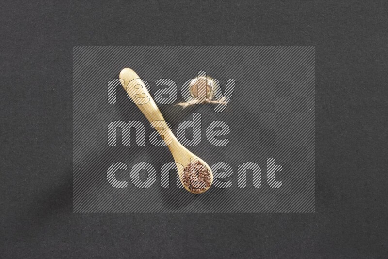 A wooden spoon full of flaxseeds with a glass bottle of flaxseeds oil on a black flooring