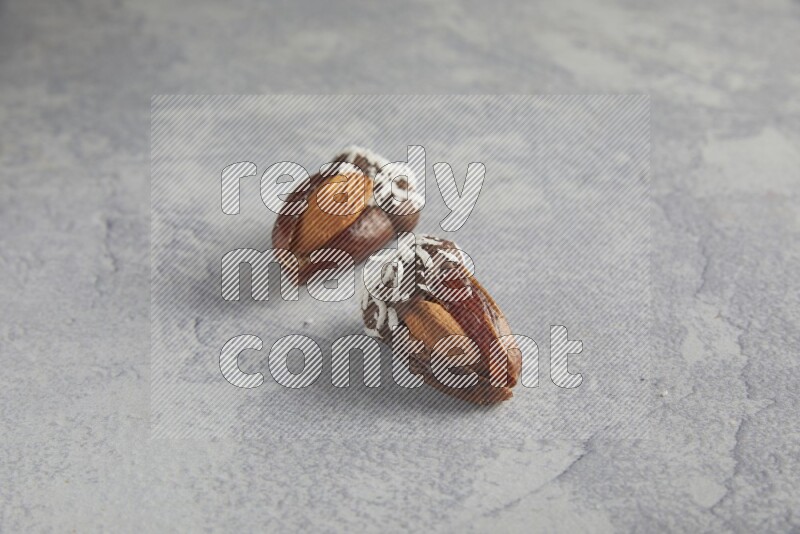 Two Almond stuffed dates covered with dark chocolate and coconut on a light grey background