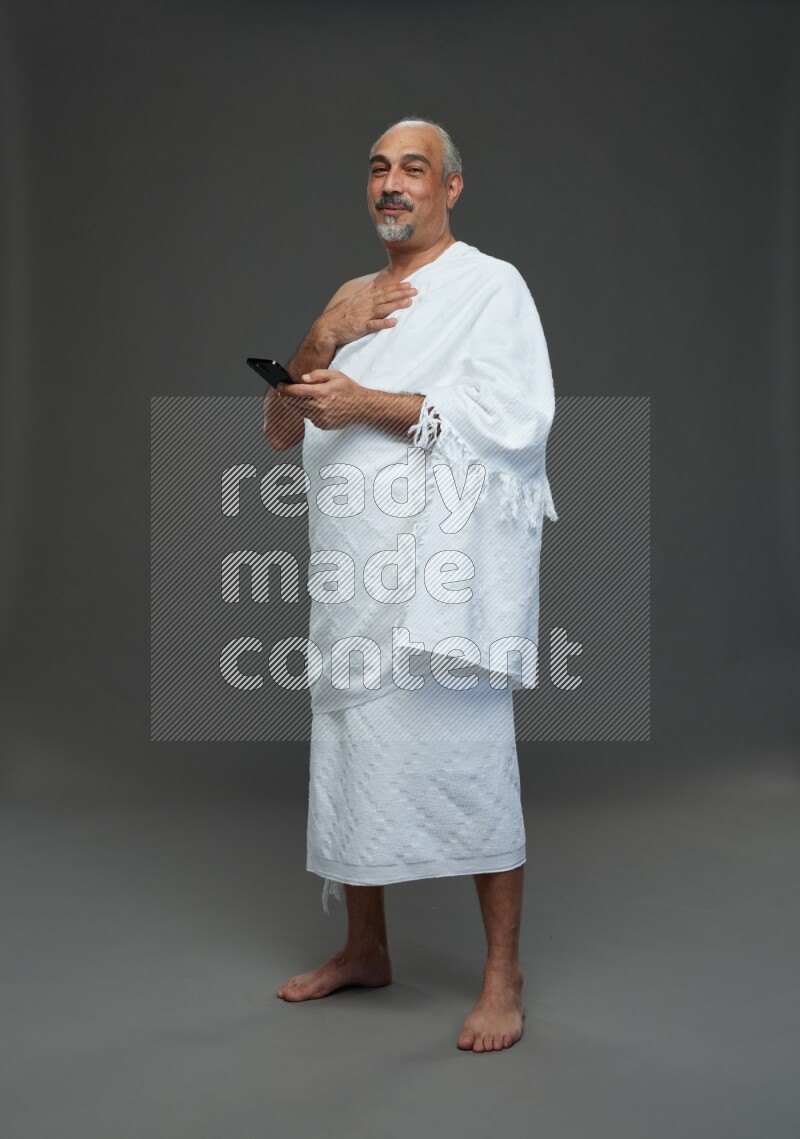 A man wearing Ehram Standing texting on phone on gray background