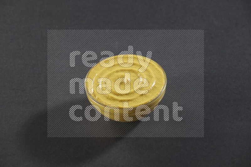 A glass bowl full of mustard paste on black flooring