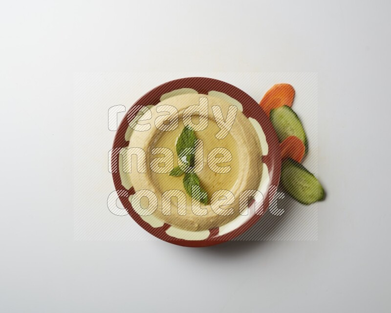 Hummus in a traditional plate garnished with mint on a white background