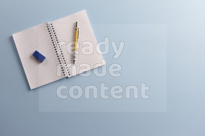 A blank open notebook with different school supplies on blue background