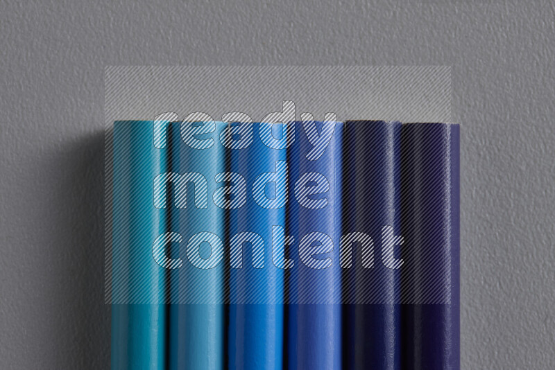 A collection of colored pencils arranged showcasing a gradient of blue hues on grey background
