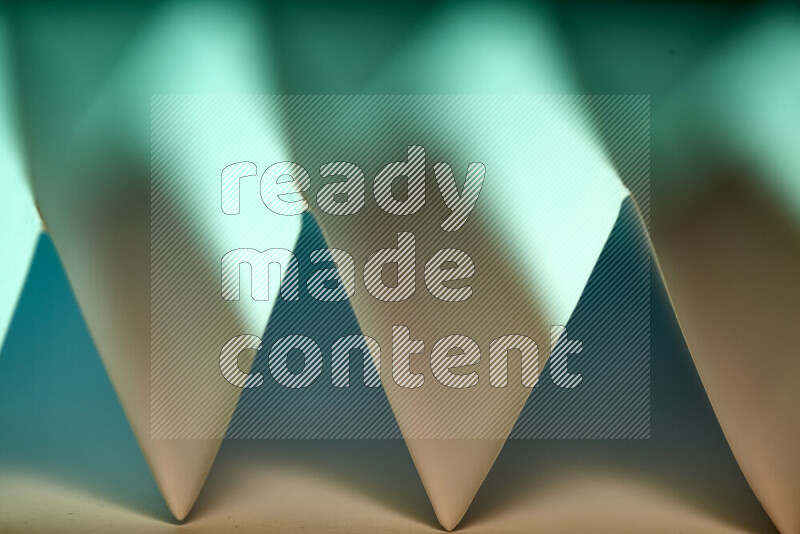 A close-up abstract image showing sharp geometric paper folds in green gradients and warm tones