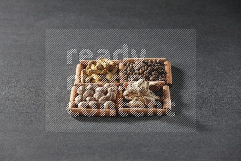 4 مربعات من عيدان القرفة ممتلئة بأصابع الكركم وبهار الفلفل الحلو والزنجبيل المجفف وجوزة الطيب على أرضية سوداء