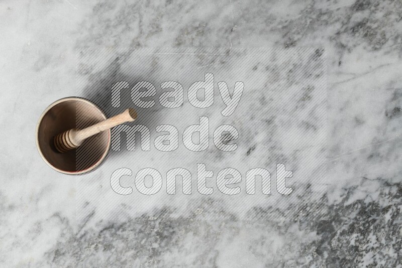 Beige pottery bowl with wooden honey dipper in it on grey marble background