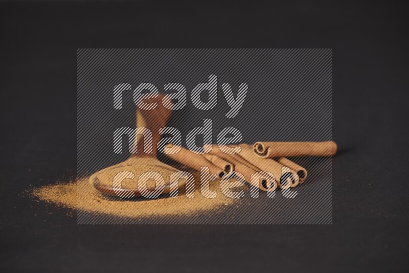 Cinnamon powder in a wooden ladle spoon with cinnamon sticks on black background