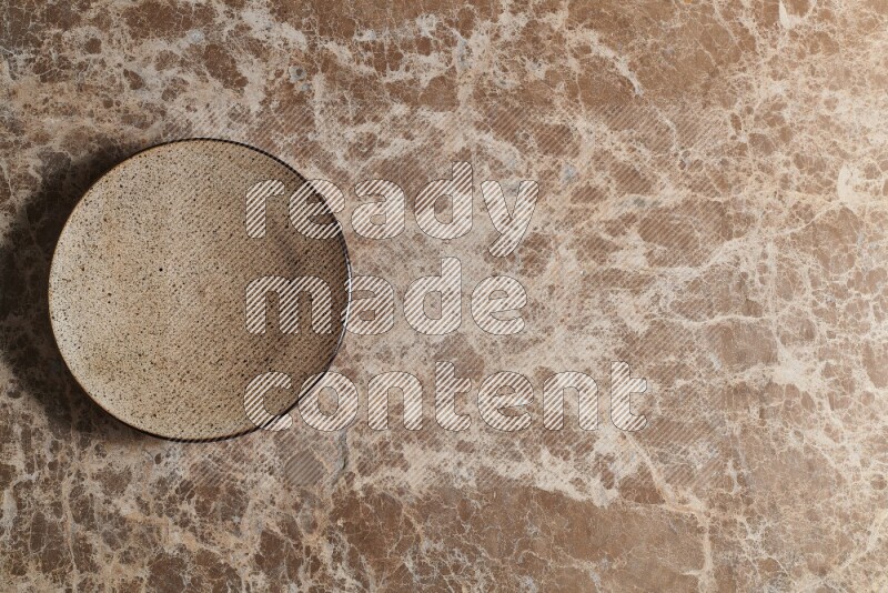 A beige pottery plate on beige marble background