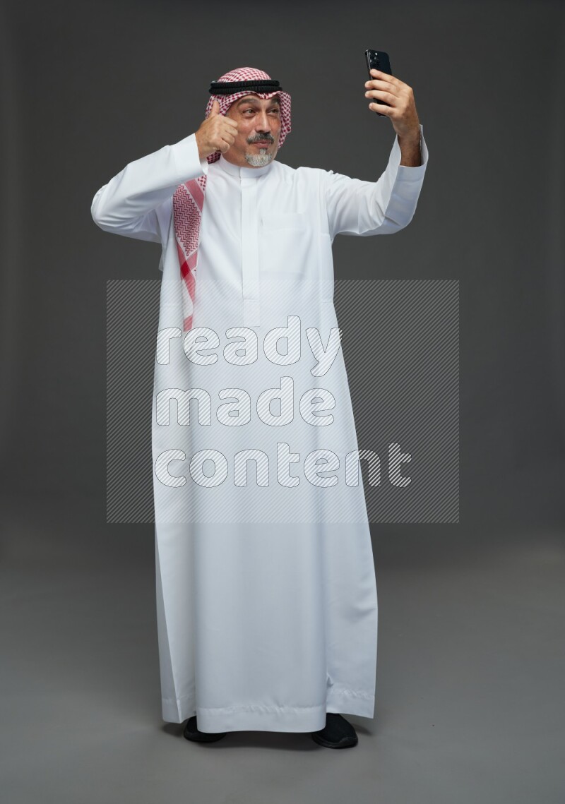 Saudi man with shomag Standing taking selfie on gray background