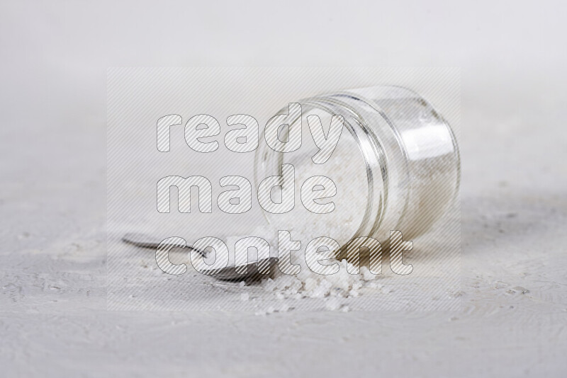 A glass jar full of coarse sea salt crystals on white background