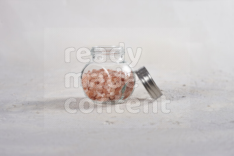 A glass jar full of coarse himalayan salt crystals on white background
