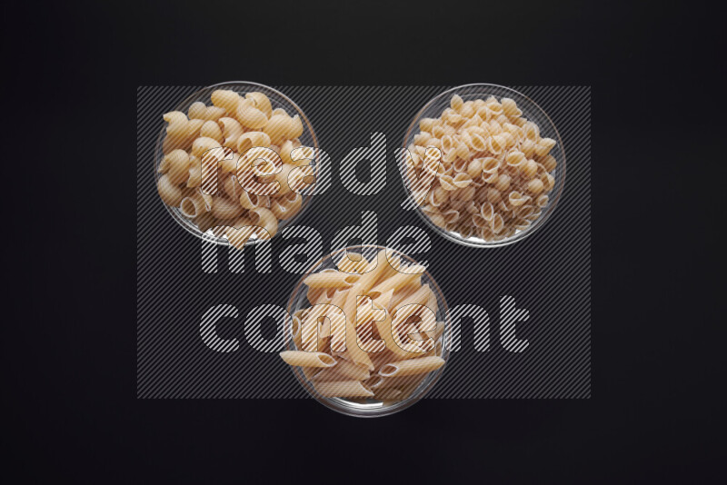 Different pasta types in glass bowls on black background
