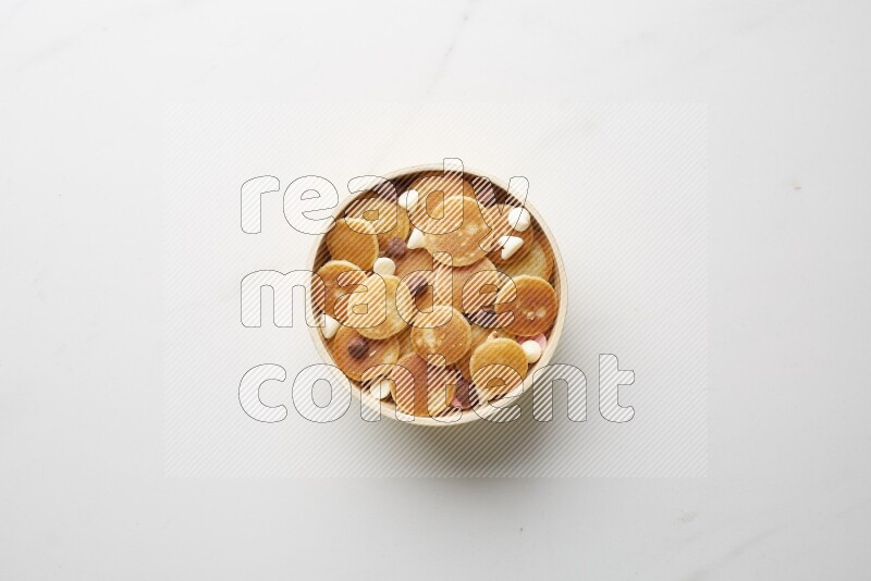 Top-view shot of mixed chocolate chips cereal pancakes in a round bowl on white background