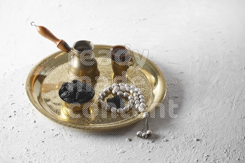 Dried plums in a metal bowl with coffee and prayer beads on a tray in a light setup