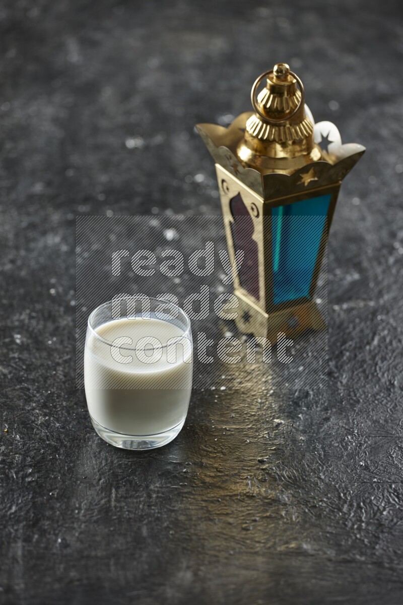 A golden lantern with different drinks, dates, nuts, prayer beads and quran on textured black background