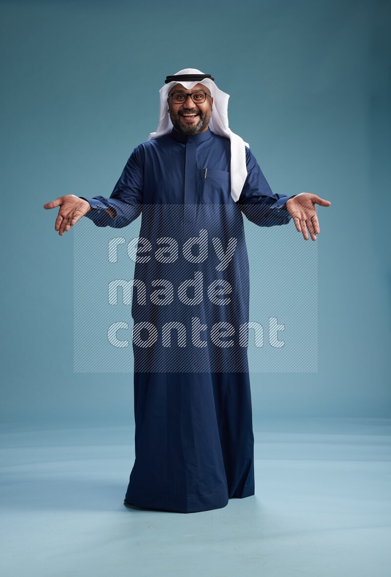 Saudi Man with shimag Standing Interacting with the camera on blue background
