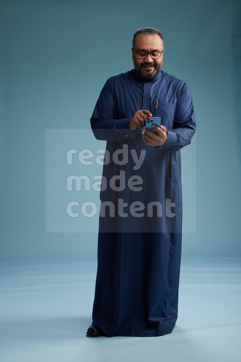 Saudi Man without shimag Standing texting on phone on blue background