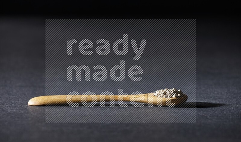 A wooden spoon full of white pepper beads on black flooring