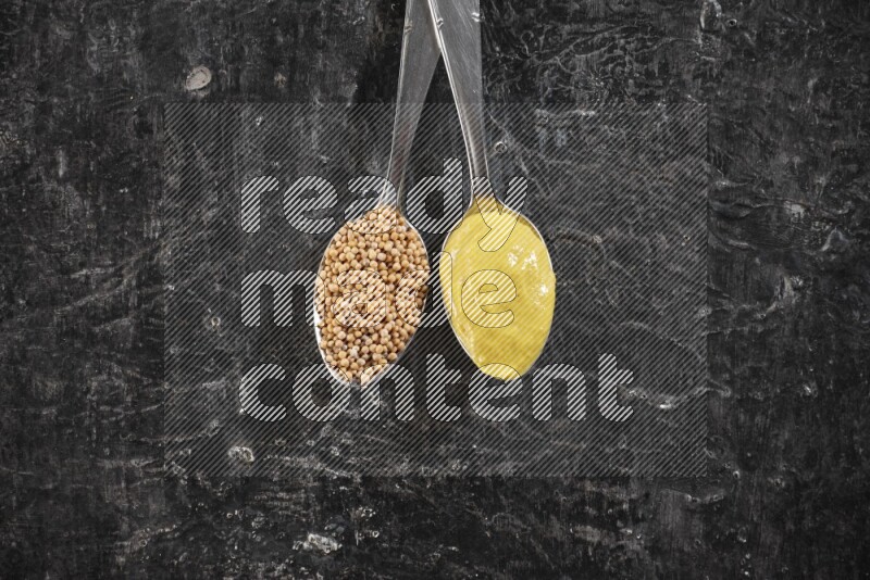 Two metal spoons, one filled with mustard seeds and the other with mustard paste on black background