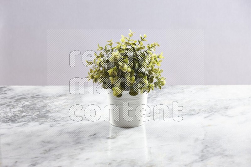 Green artificial plant in white pot on light grey marble background