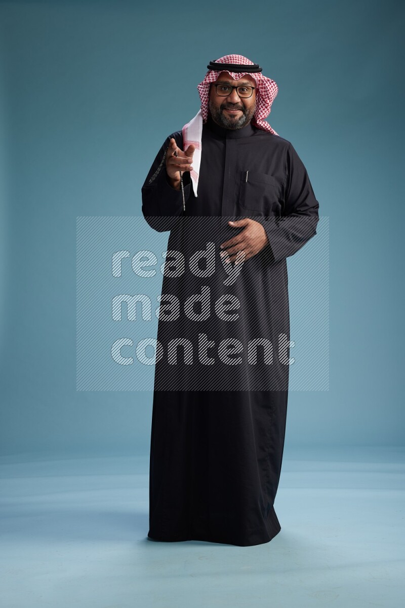 Saudi Man with shimag Standing Interacting with the camera on blue background