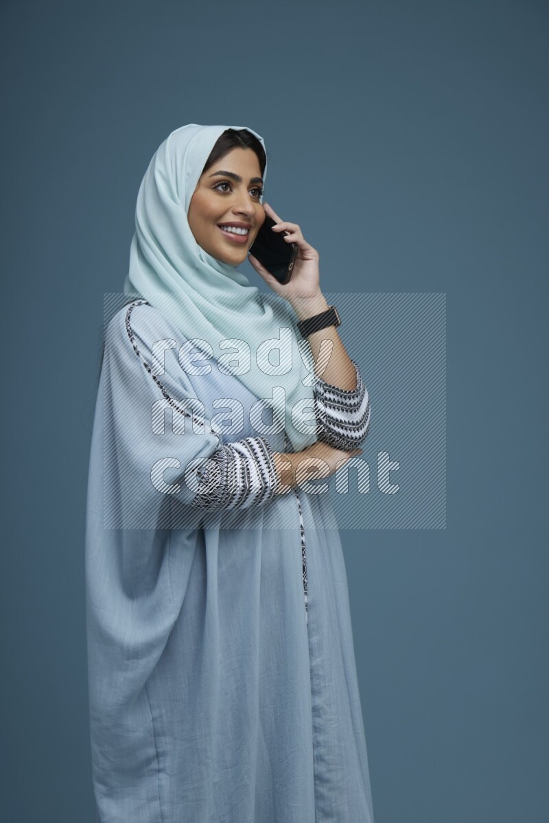 A Saudi woman having a Call in a blue background wearing blue Abaya with hijab