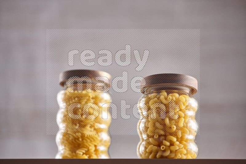 Raw pasta in glass jars on beige background