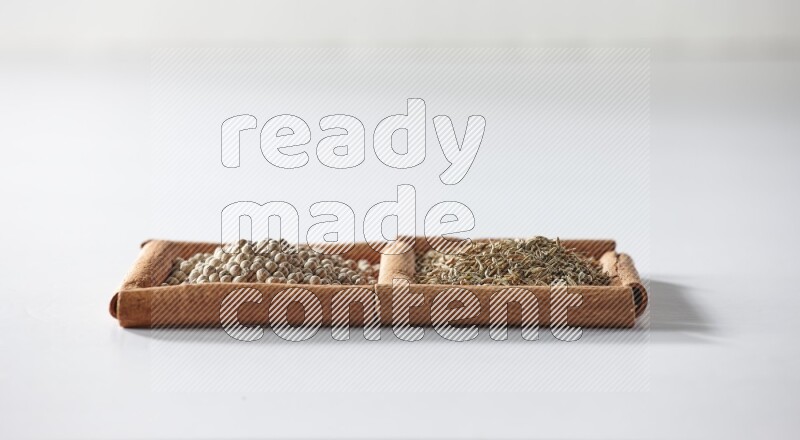 مربعان من أعواد القرفة ممتلئان بحبوب الفلفل الأبيض وحبوب الكمون علي خلفية بيضاء