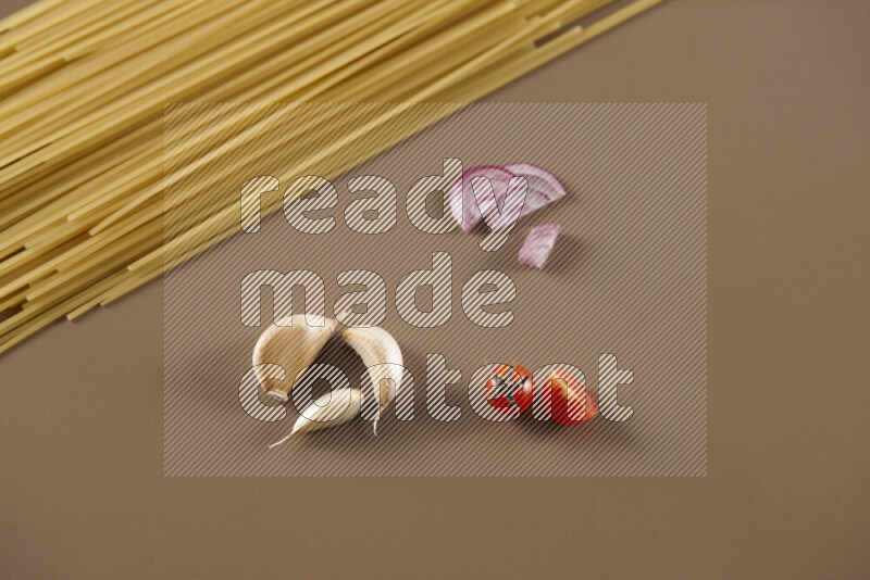 Raw pasta with different ingredients such as cherry tomatoes, garlic, onions, red chilis, black pepper, white pepper, bay laurel leaves, rosemary and cardamom on beige background