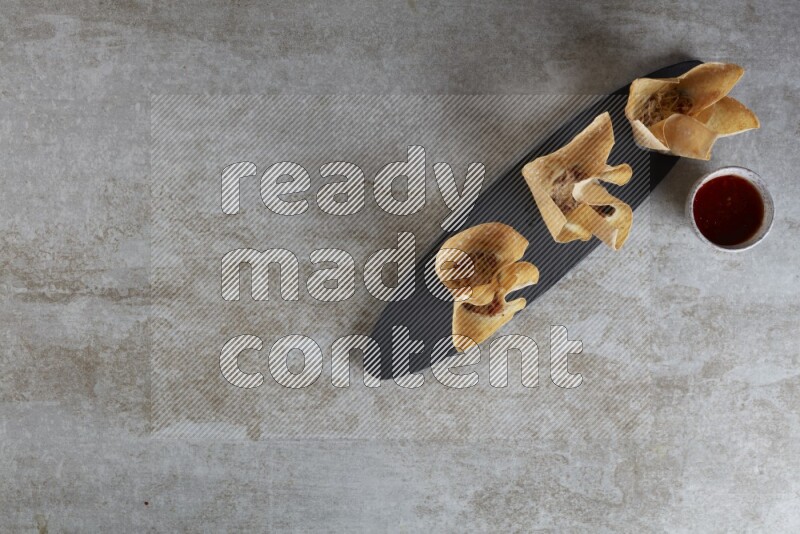 wonton cups with soy sauce ramkin on oval slate on grey textured counter top