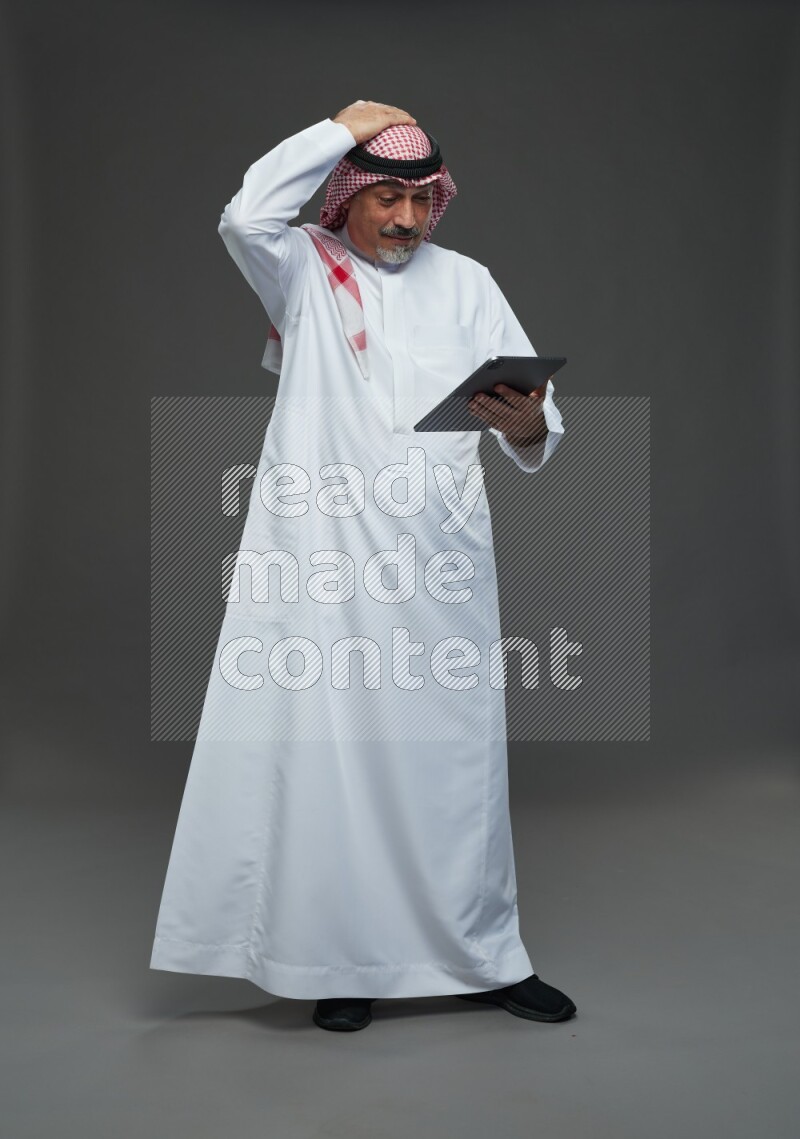 Saudi man with shomag Standing working on tablet on gray background