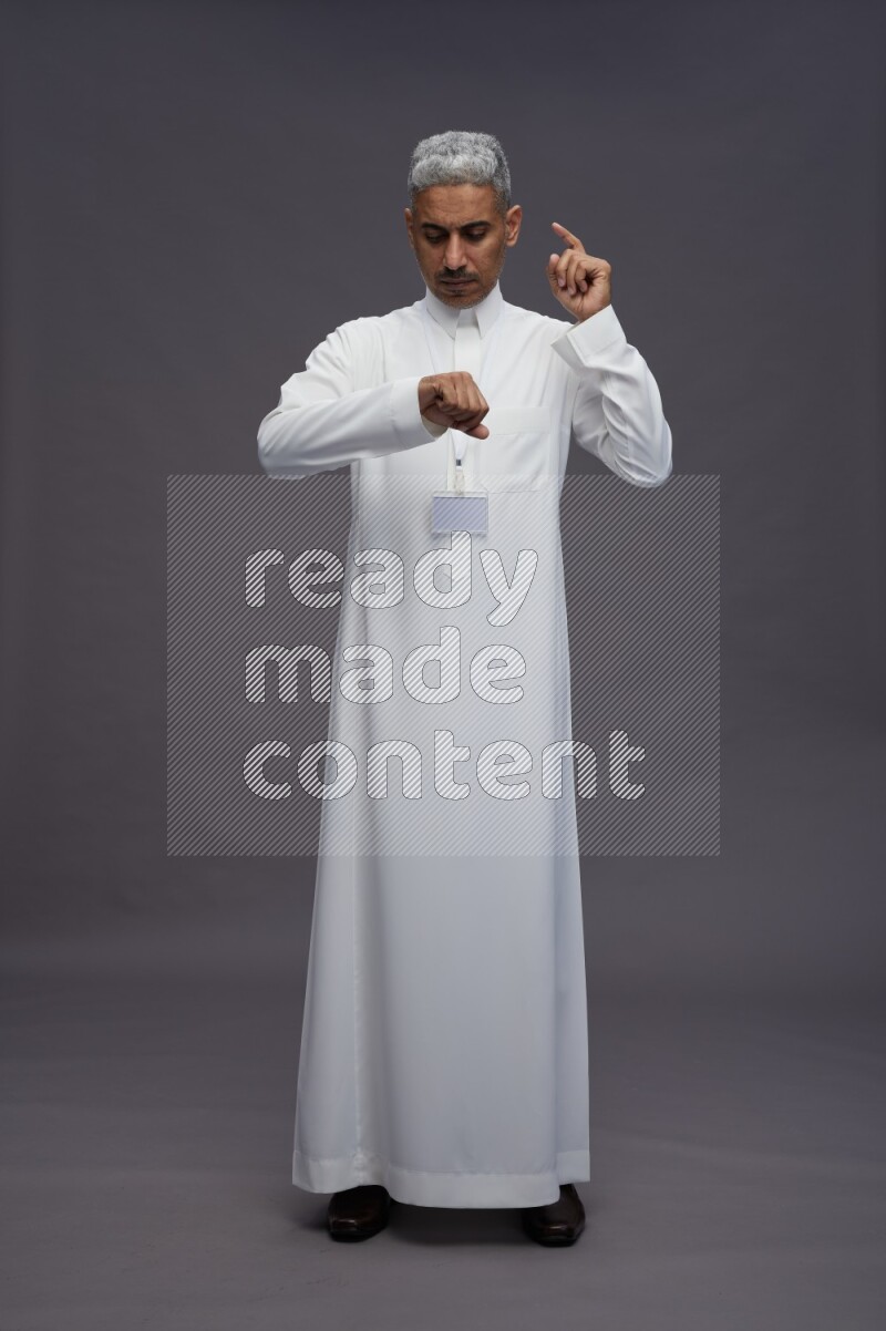 Saudi man wearing thob with neck strap employee badge standing interacting with the camera on gray background