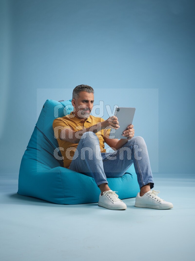 A man sitting on a blue beanbag and working on tablet
