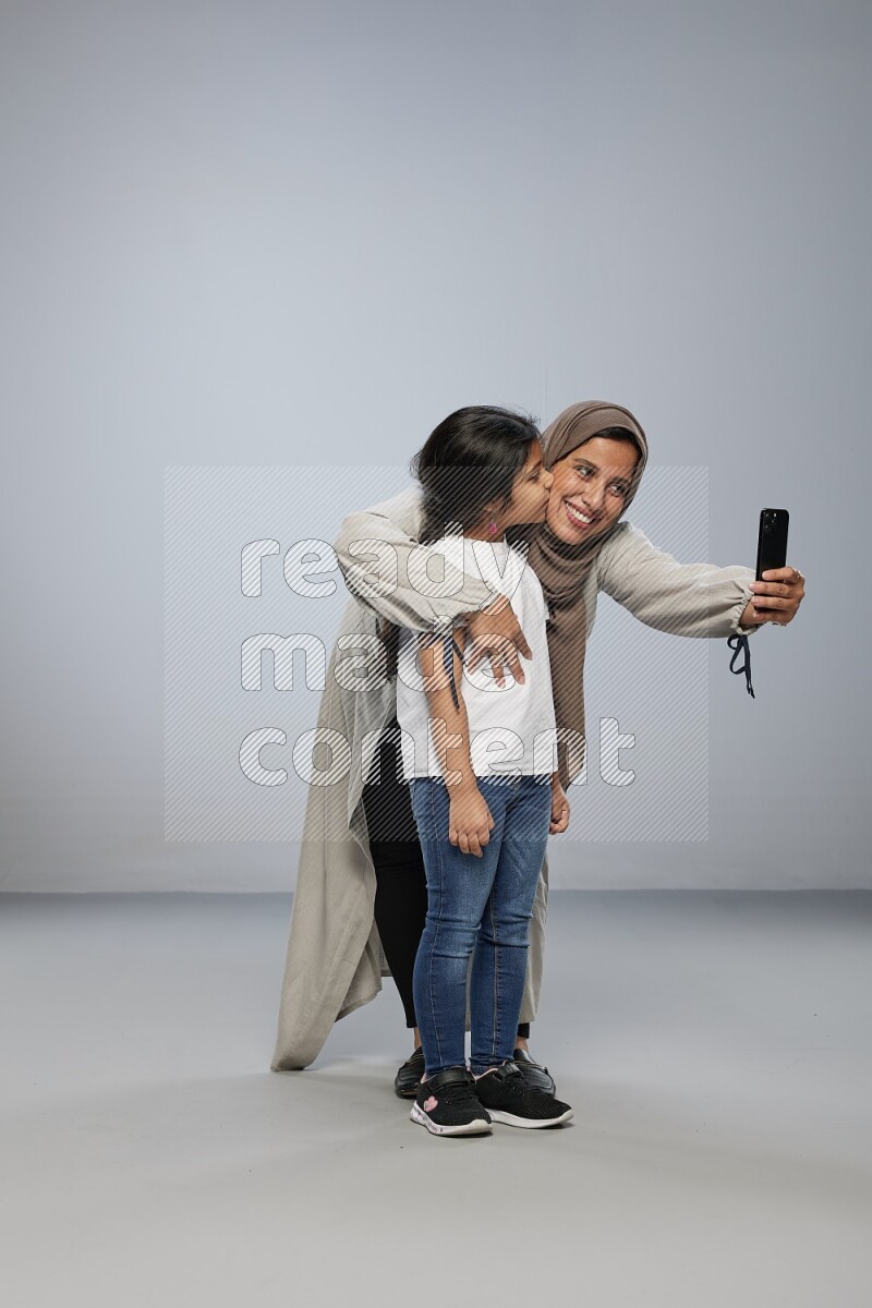 A girl standing taking selfie with her mother on gray background