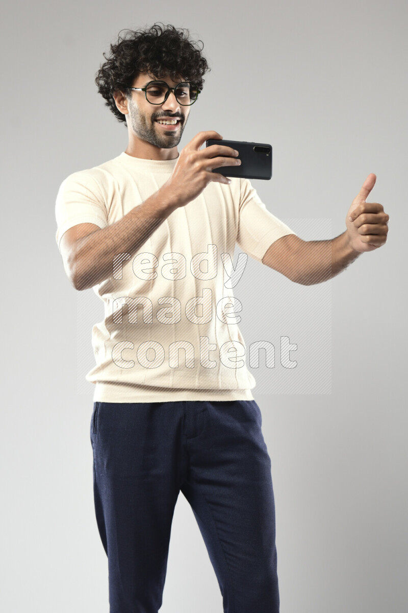 A man wearing casual standing and shooting with his phone on white background