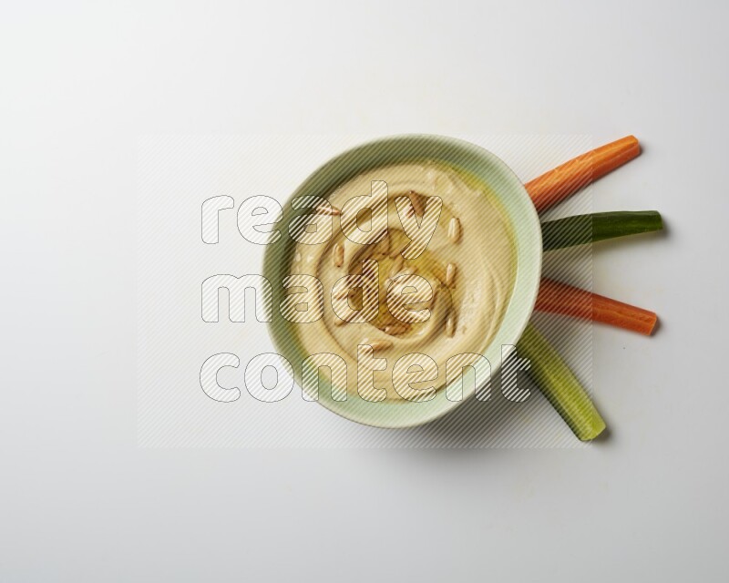 Hummus in a green plate garnished with pine nuts on a white background