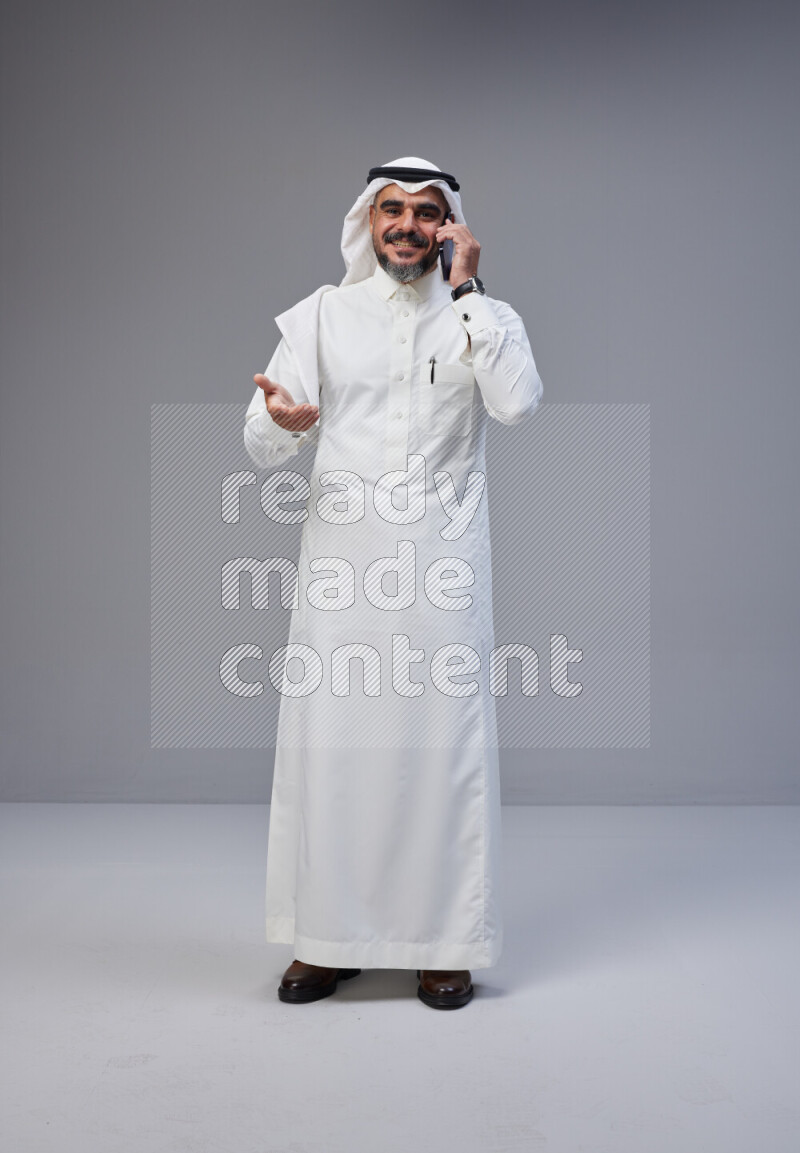 Saudi man Wearing Thob and white Shomag standing talking on phone on Gray background