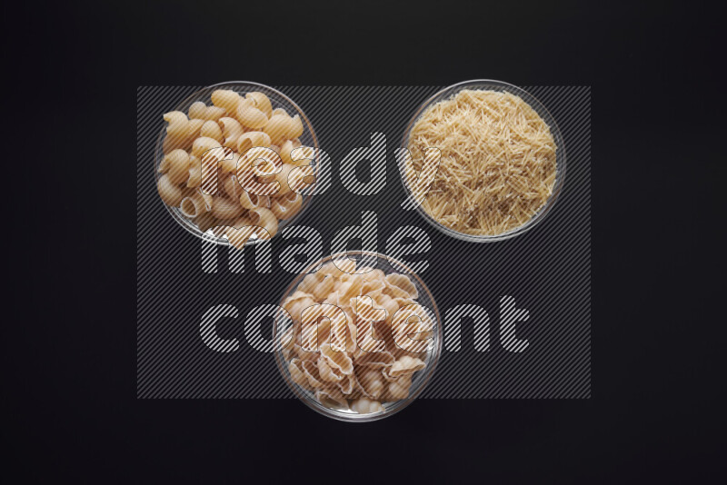 Different pasta types in glass bowls on black background