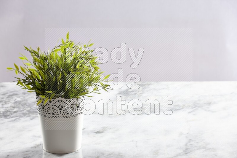 Green artificial plant in white decorative pot on grey marble background