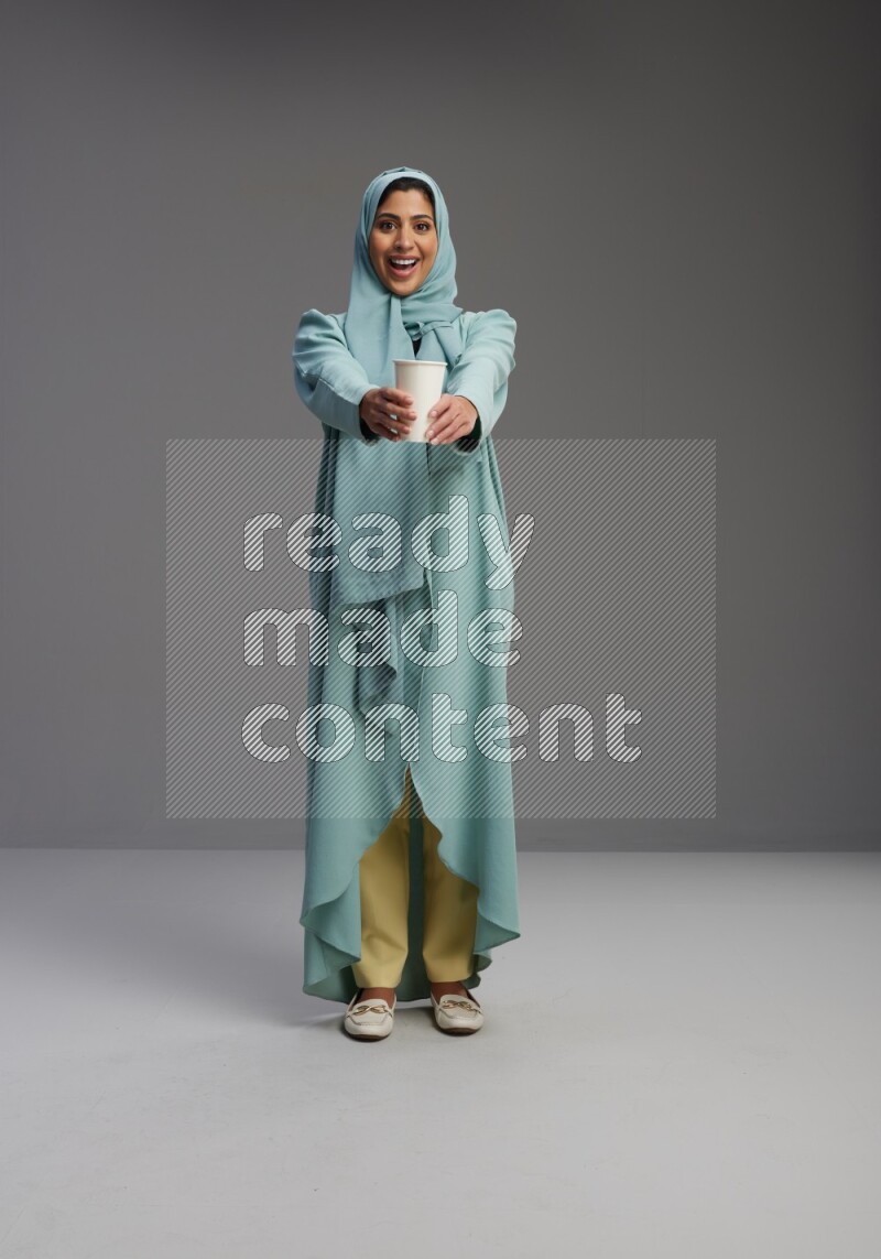 Saudi Woman wearing Abaya standing  holding paper cup on Gray background
