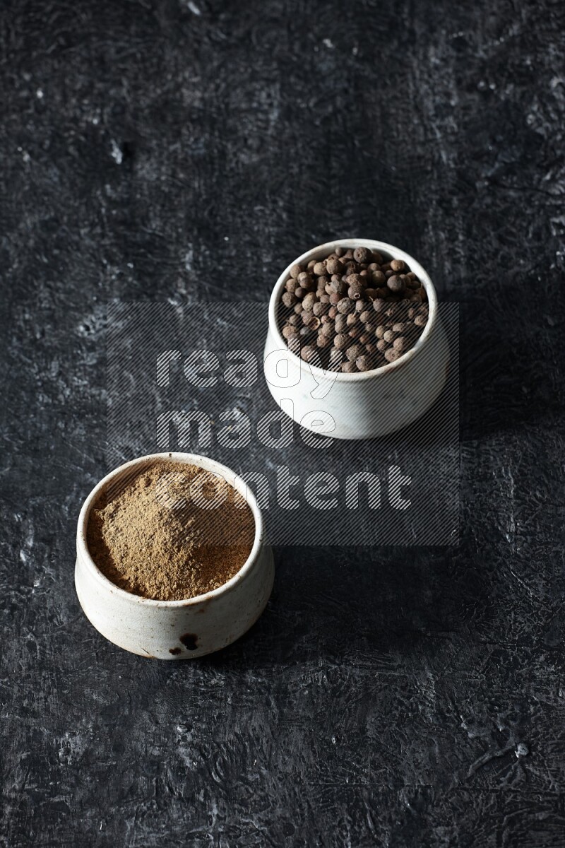 وعاءان بيج، أحدهما ممتلئ ببودرة بهار الفلفل الحلو والآخر بالحبوب على خلفية سوداء